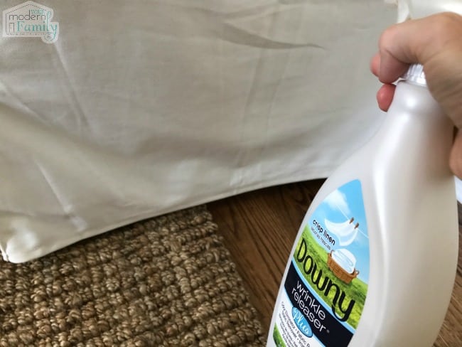 A hand spraying a bottle of Downy  Wrinkle Releaser on a white slip cover.