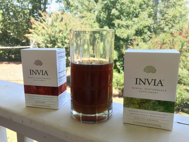 A glass of Invia  with two boxes of Invia on each side.