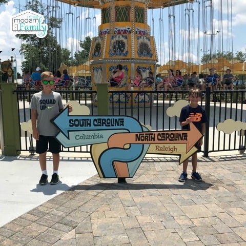 Two boys standing beside a sign with a carousel behind them.
