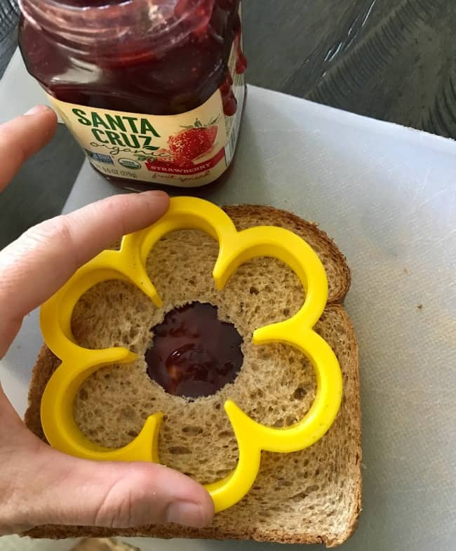 A peanut butter and jelly sandwich with a flower cookie cutter being pressed into it.