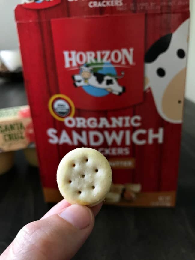A hand holding a Horizon cracker with the box behind it.