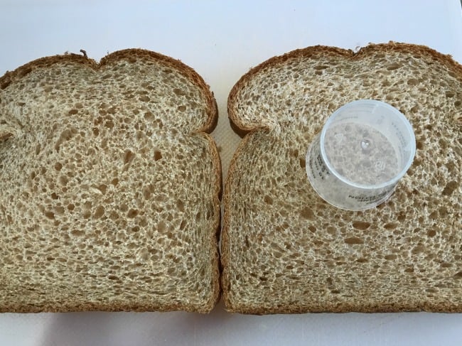 A close up of  two slices of bread with a plastic cup resting on one of the slices.