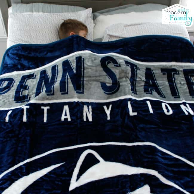 A boy sleeping in a bed with a football themed blanket.