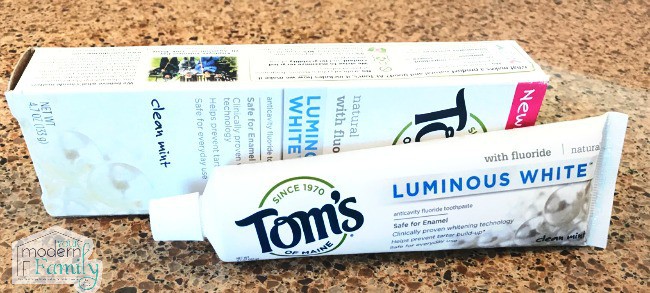 A tube of Tom\'s tooth paste lying on a counter with it\'s box behind it.