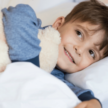 A boy holding a teddy bear lying on a bed.