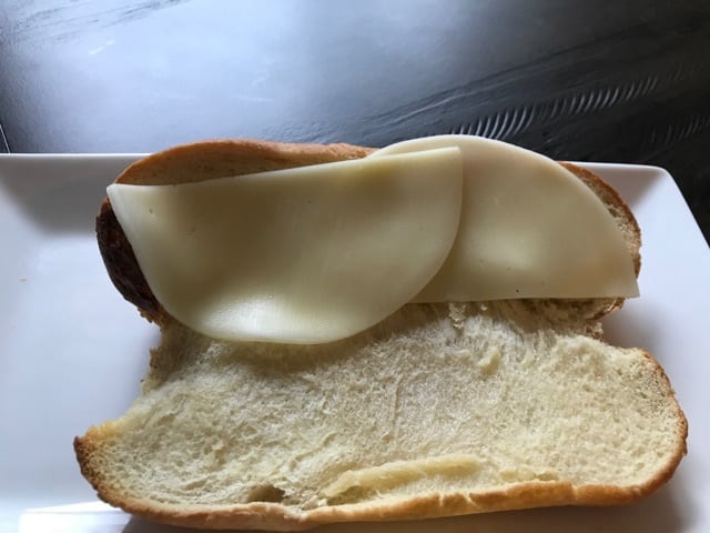 A close up of a sandwich roll with provolone cheese on it.