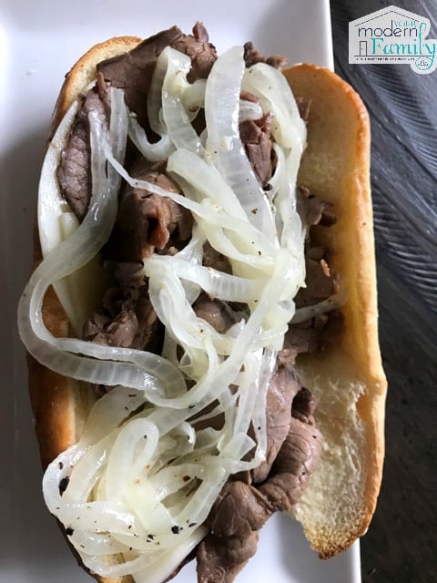 A close up of a roast beef dip sandwich with onions on it.