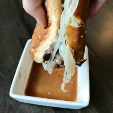 A person's hand dunking a sandwich into gravy.