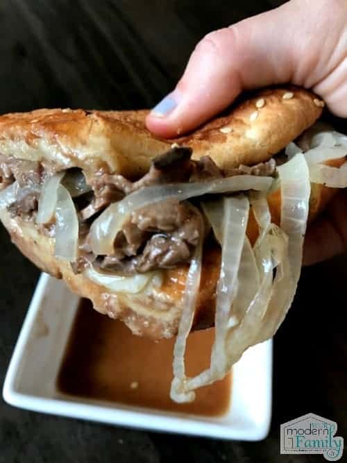 A close up of a hand holding a roast beef dip sandwich.