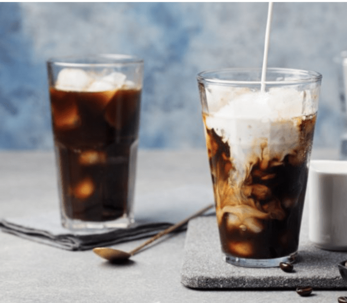 A close up of two glasses of iced coffee as someone is pouring cream into one.