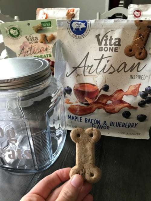 A variety of bags of Vita Bone Artisan dog treats and a class jar sitting on a table.