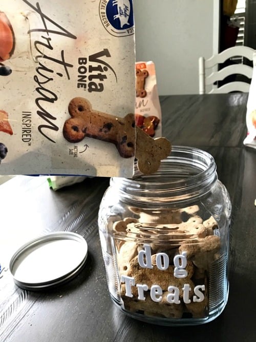 A glass jar with dog treats being poured into it.