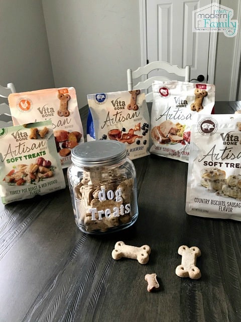 A variety of bags of Vita Bone dog treats and a filled dog treat jar sitting on a table.