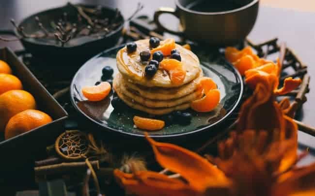 A large stack of pancakes with oranges and blueberries on them.