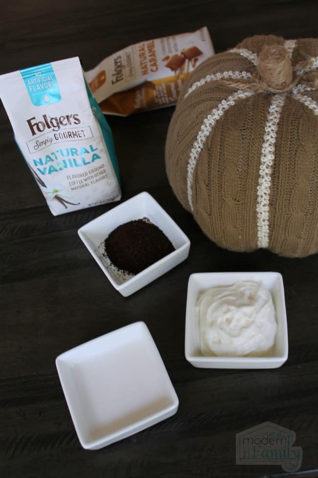 Two flavors of Folgers coffee with some of the product poured into a white square bowl and a pumpkin beside it.
