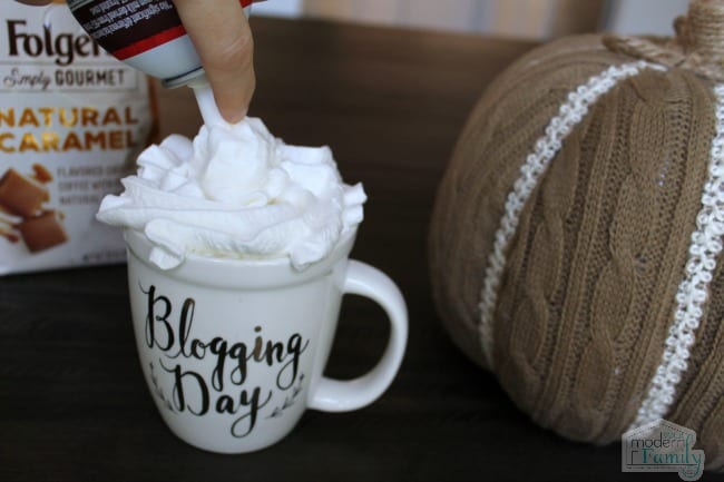A cup of coffee on a table as whipped cream is added to it.