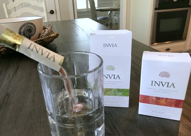 Invia packet being poured into a glass of water with two boxes of Invia behind it.