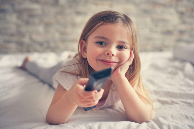 A little girl sitting on a bed holding a remote control.