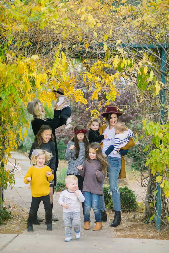 A group of young children and two adults standing under a tree together.