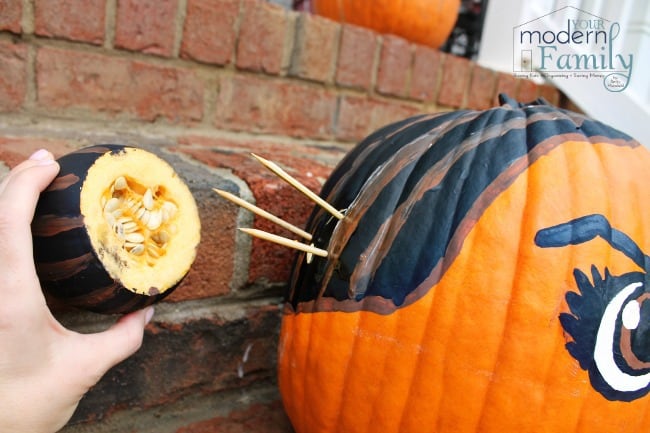 A person putting a decoration onto a pumpkin sitting on the front steps.