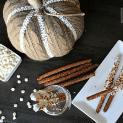 Cinnamon sticks on a white plate with a pumpkin decoration beside them on a wooden table.