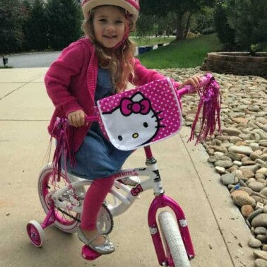 A little girl riding a bike in the driveway.