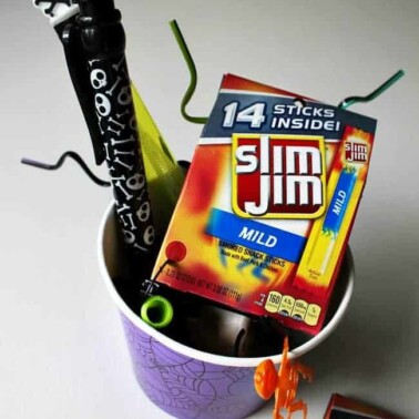A purple bucket with a variety of Halloween treats in it.