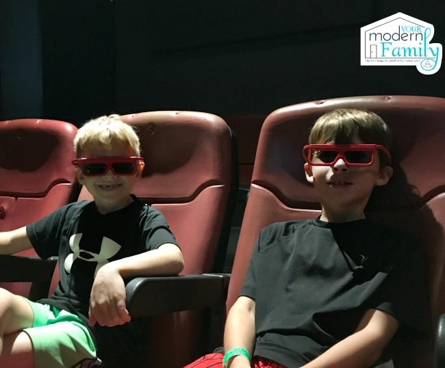 Two boys sitting in a movie theater with 3D glasses on.