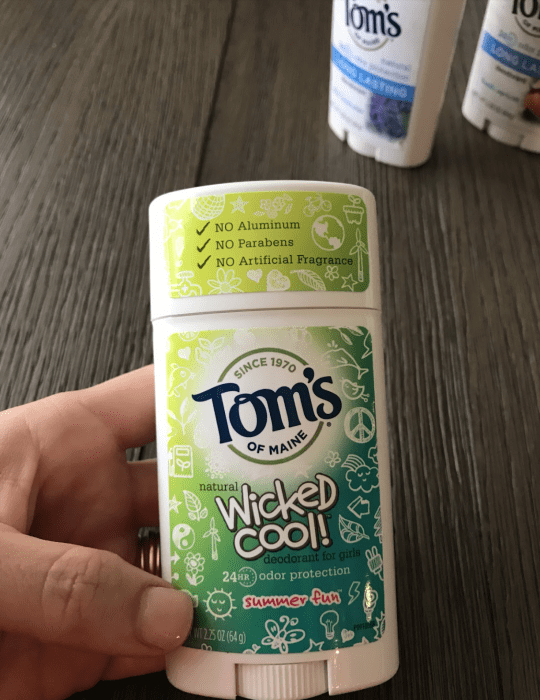 A hand holding a container of Tom\'s deodorant.