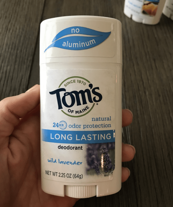 A hand holding a container of Tom\'s deodorant.