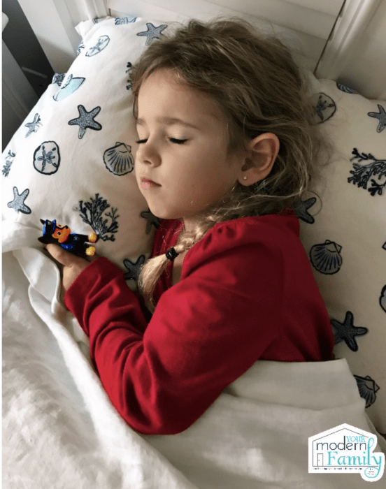 A little girl sleeping in bed holding a Paw Patrol toy.