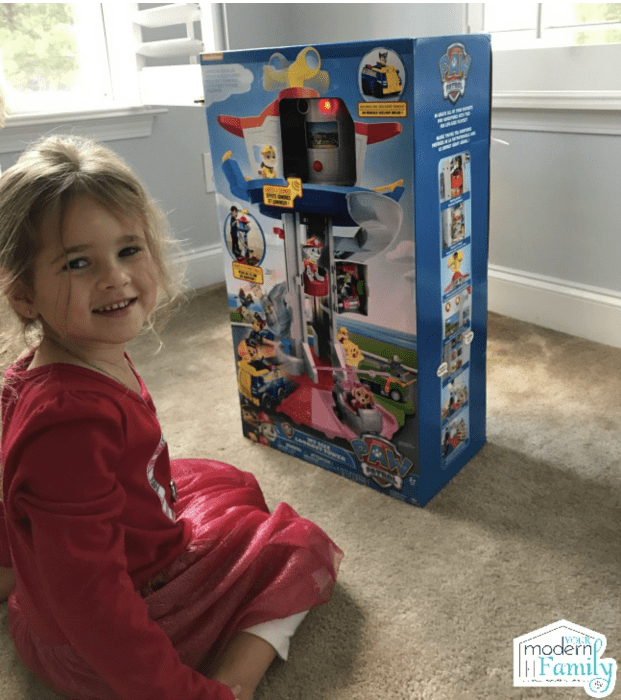 A little girl sitting in front of a Paw Patrol box.