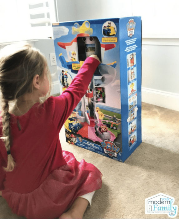 A little girl sitting on the floor looking at a Paw Patrol toy.