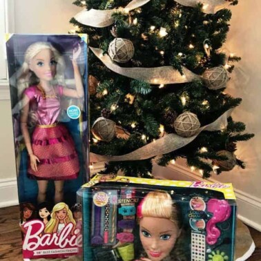 A Christmas tree with unopened Barbie Dolls under it.