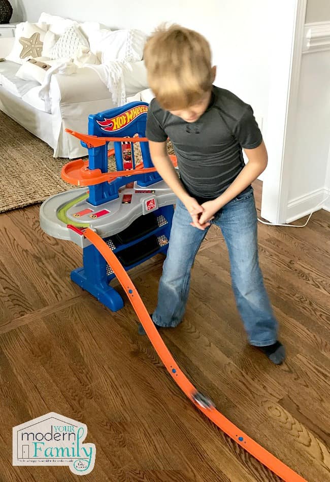 A little boy playing with a Hot Wheel\'s track.