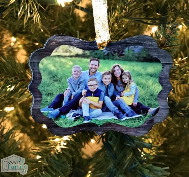 A Christmas ornament frame with a family portrait hanging from the tree. 