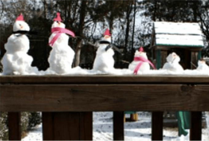 Miniature snowmen sitting on a porch railing.