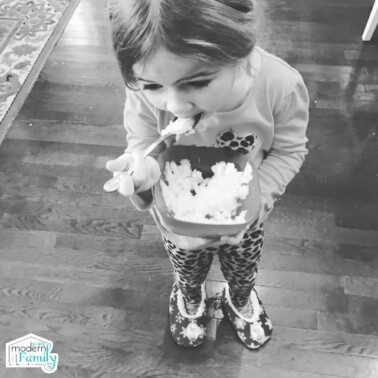 A little girl holding a bowl and eating with a spoon.