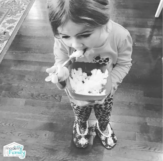 A little girl holding a bowl and eating with a spoon.