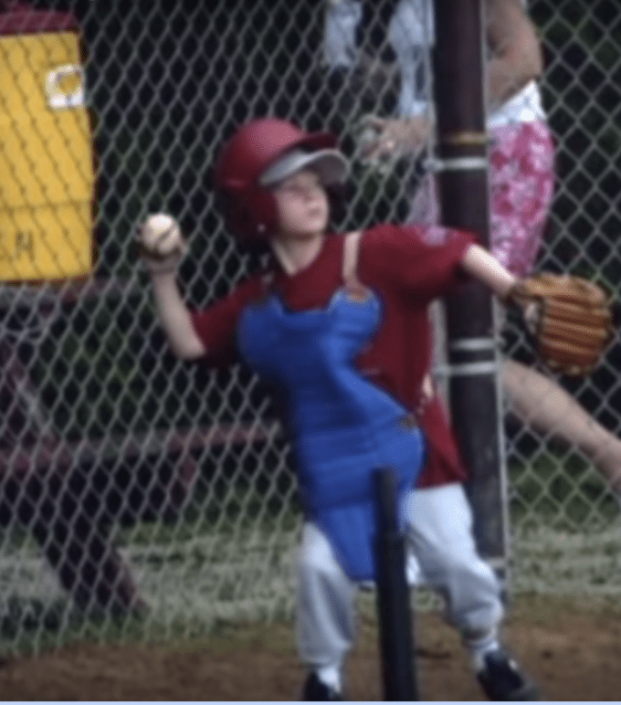 A young boy throwing a baseball with a catcher's equipment on.