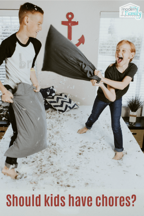 Two kids standing on a bed having a pillow fight.