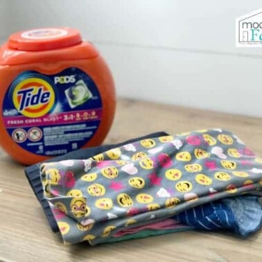 A container of Tide Pods detergent beside colorful children's clothes neatly folded.