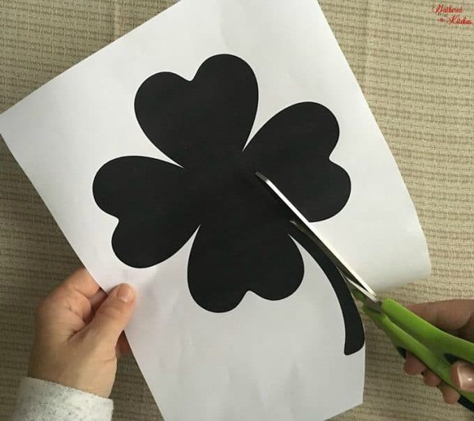 A person cutting out a black shamrock for a craft project.