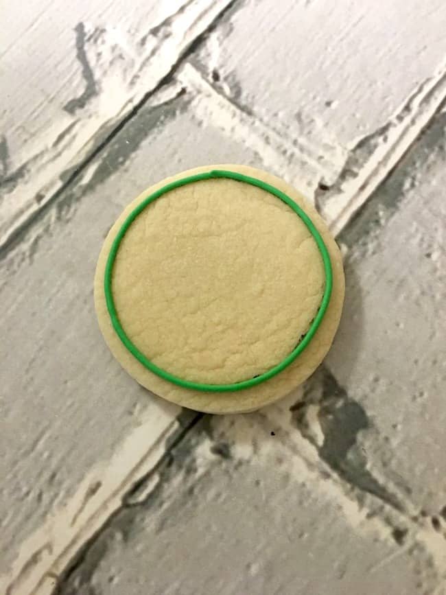 Close up of a round sugar cookie with green icing around the rim of the cookie.
