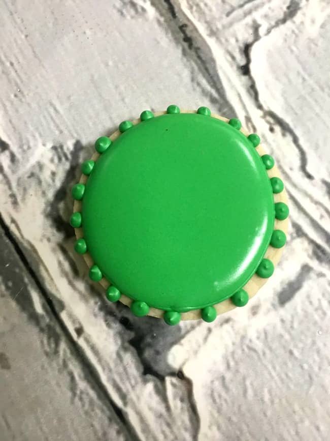 A green iced sugar cookie with green dots around the rim of the cookie.