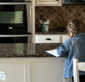 A little girl sitting at the kitchen counter doing paper work.