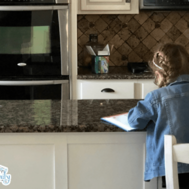 A little girl sitting at the kitchen counter doing paper work.