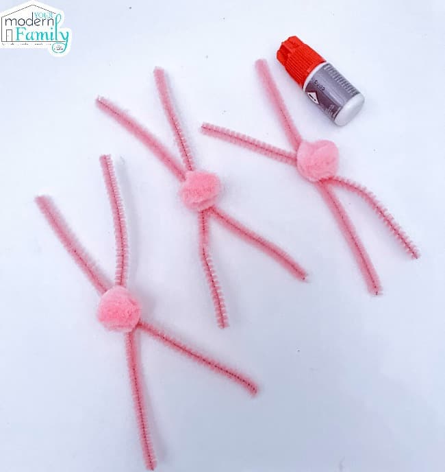 Three sets of crisscrossed pipe cleaners with a pink fuzzy ball glued on to each one.