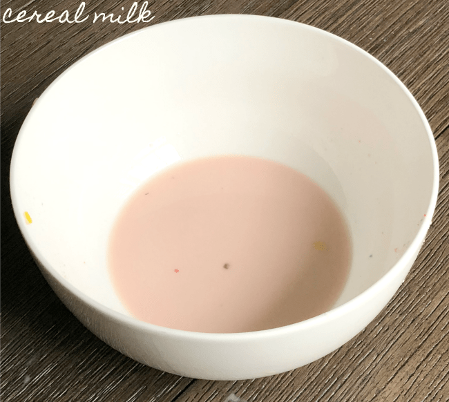 A white bowl sitting on a table with  cereal milk in it.