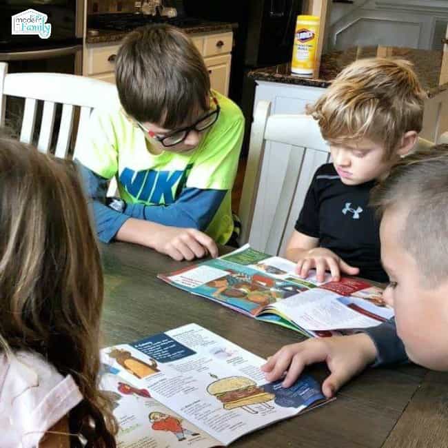 Children sitting at a table looking at magazines together.